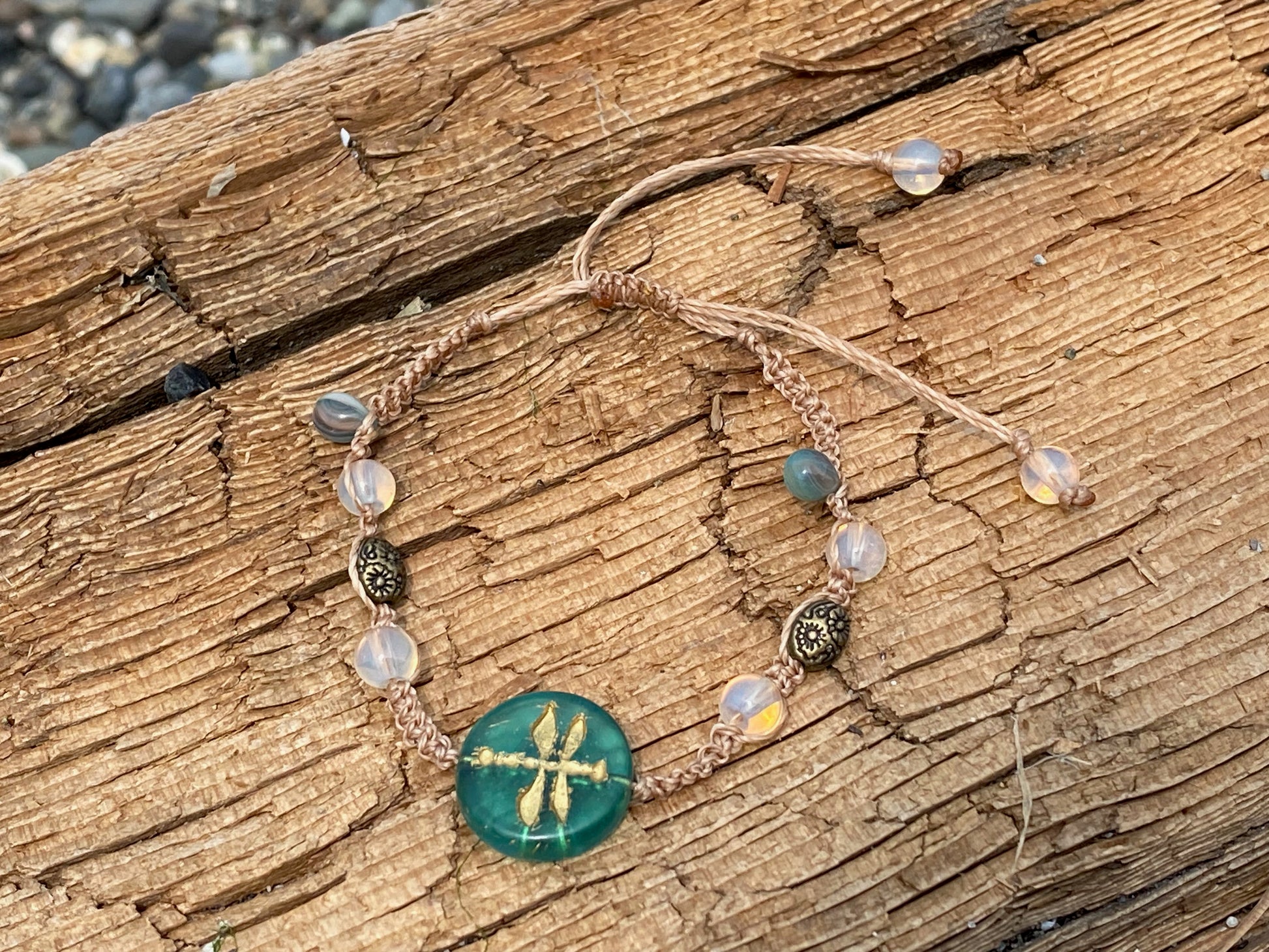 Beautiful Woven bracelet with aqua dragonfly coin bead , sparkle beads, antique copper beads on a piece of driftwood by the ocean