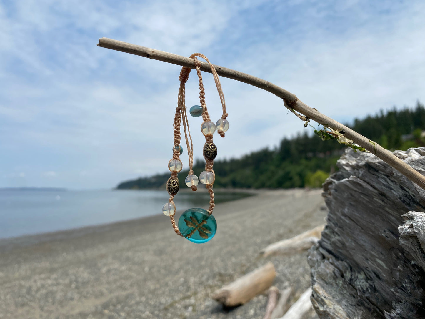 Beautiful Woven bracelet with aqua dragonfly coin bead , sparkle beads, antique copper beads on a piece of driftwood by the ocean
