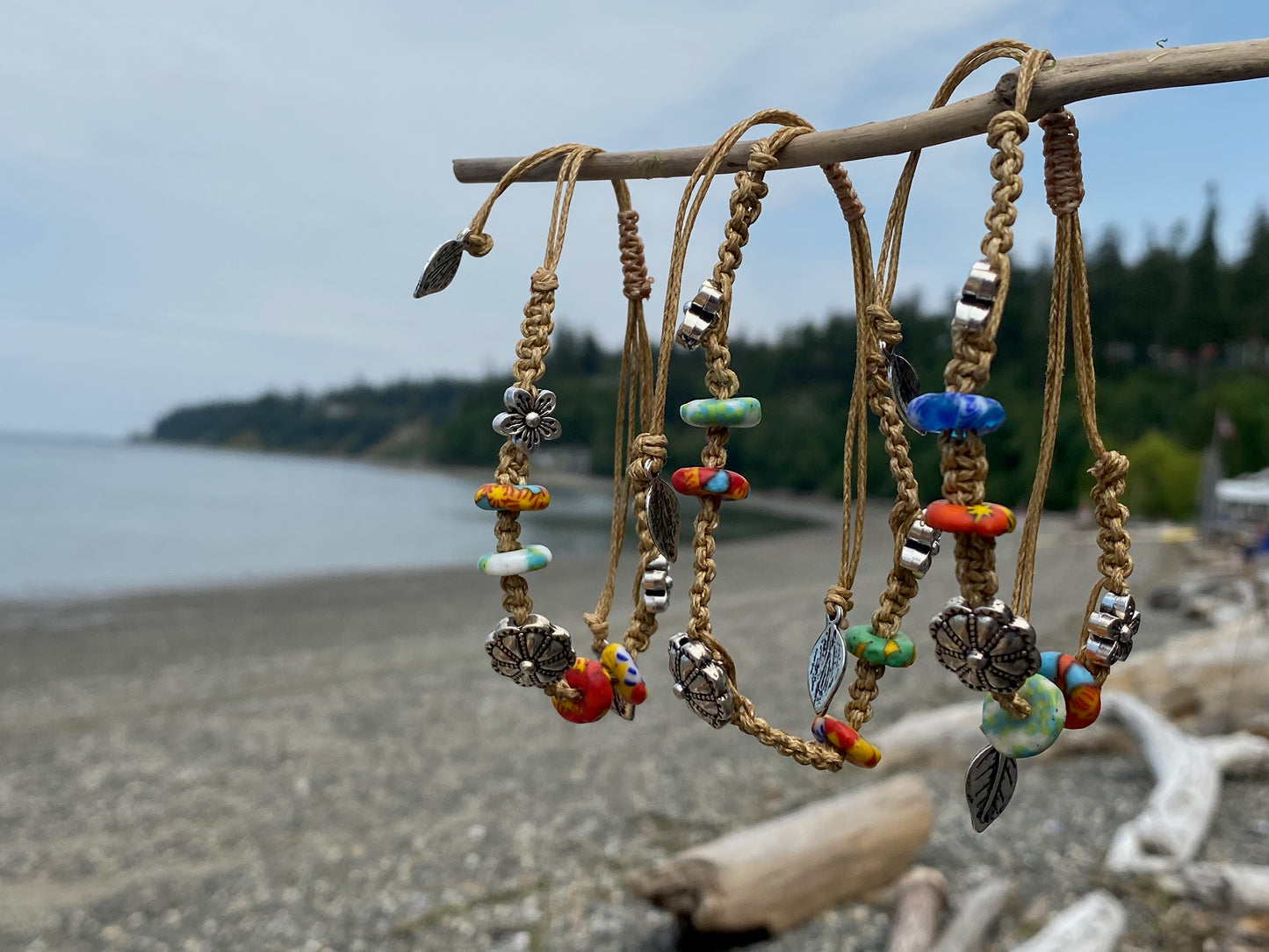 Beautiful woven bracelets with silver beads and african beads, hanging on a piece of driftwood by the ocean