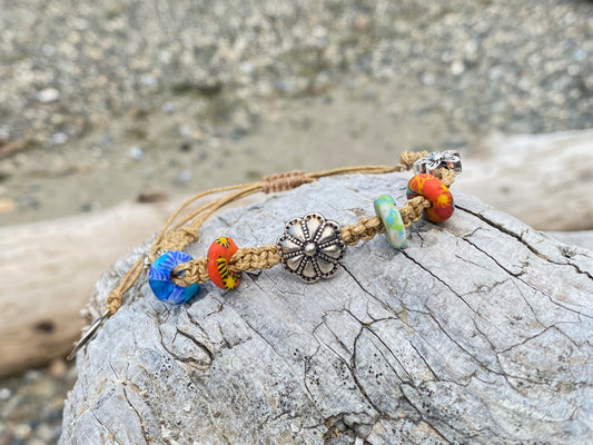 Beautiful woven bracelet with silver beads and african beads, on a piece of driftwood by the ocean
