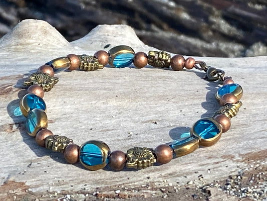 This beautiful beach bracelet on a piece of driftwood, The bracelet is adorned with copper colored beads that add a warm, rustic touch to the overall design. Antique brass colored sunflowers give the piece a vintage feel, while also symbolizing warmth, happiness, and longevity.