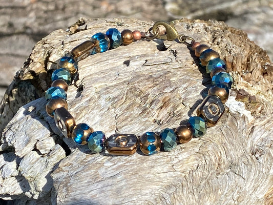 a a beautiful  beach bracelet on a piece of driftwood with a combination of copper, clear glass beads encased in copper, and sparkly blue-green ocean color beads, 